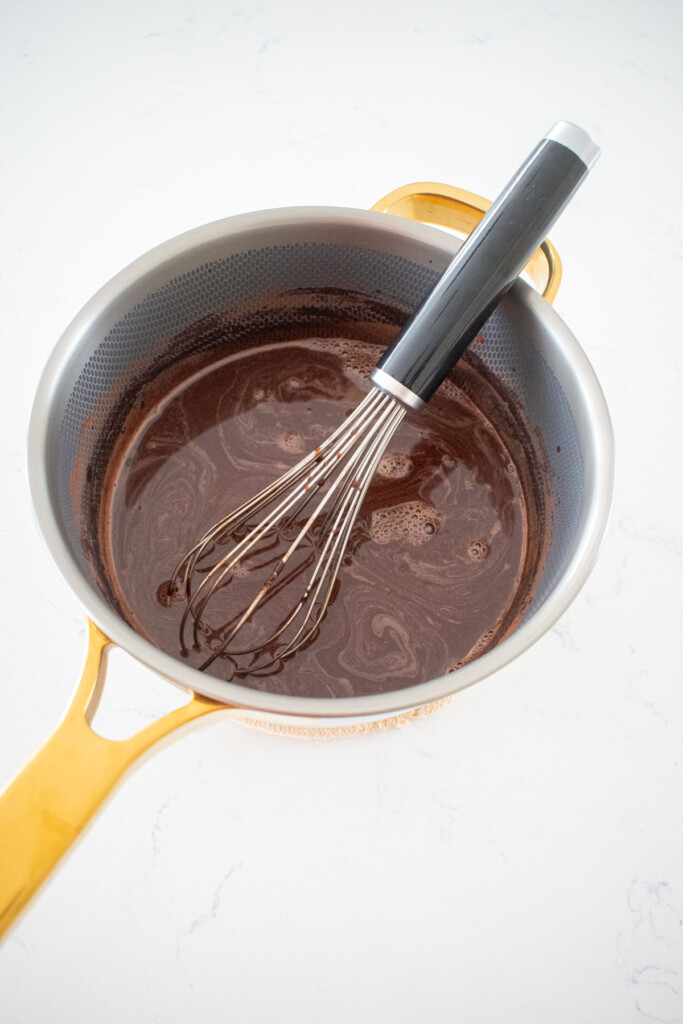 chocolate protein pudding in a small pot with a whisk on a marble counter.