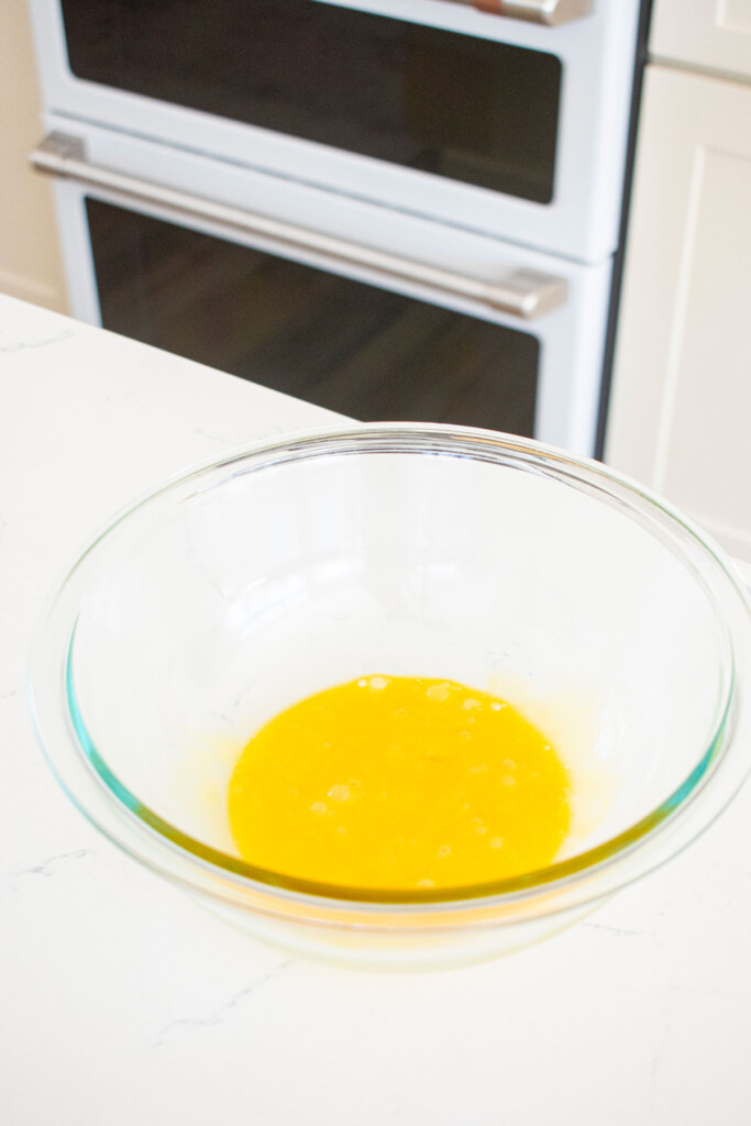 egg yolks in a glass mixing bowl on a white marble counter.