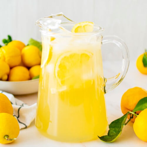 organic homemade lemonade in a glass pitcher with fresh lemons on a marble countertop.