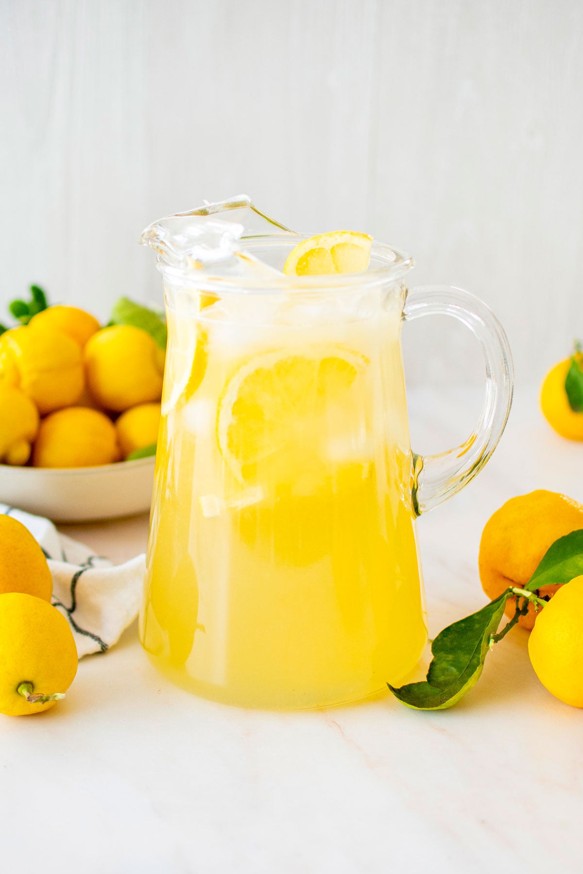 organic homemade lemonade in a glass pitcher with fresh lemons on a marble countertop.
