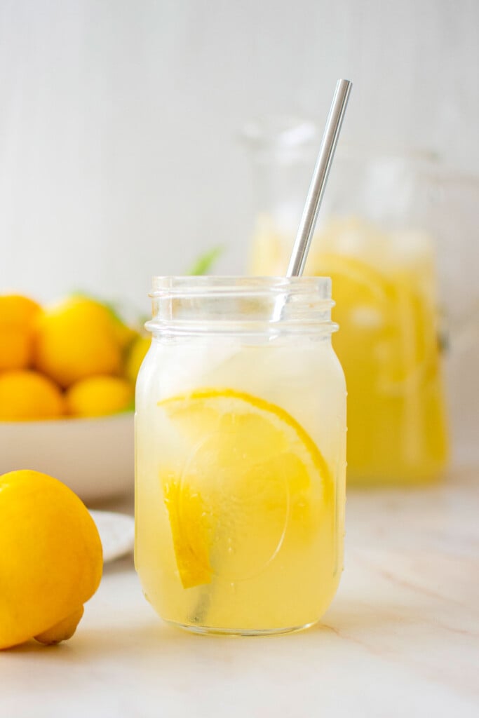 organic homemade lemonade in a mason jar glass with a metal straw on a marble countertop.