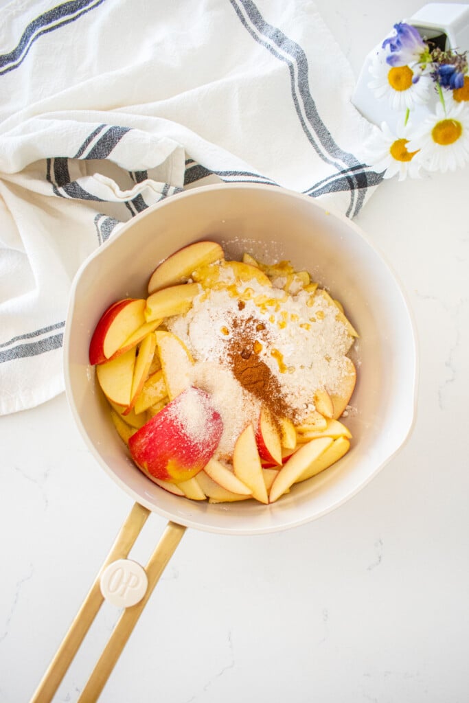 small pot with sliced apples, sugar, honey, flour, lemon juice, zest and cornstarch on a marble counter.