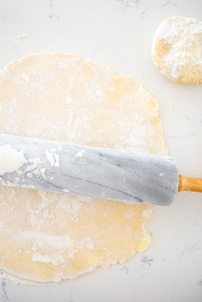 butter pie crust being rolled out on a marble counter with a marble rolling pin.