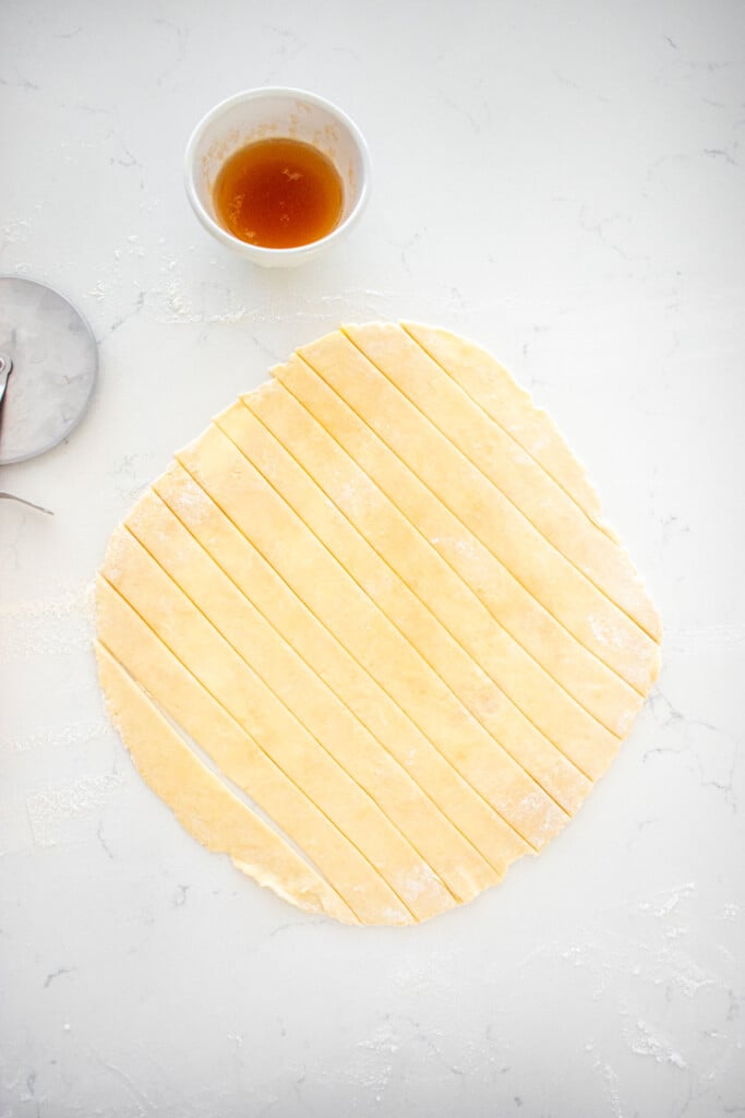 top pie crust cut into 1-inch thick strips on a marble counter.