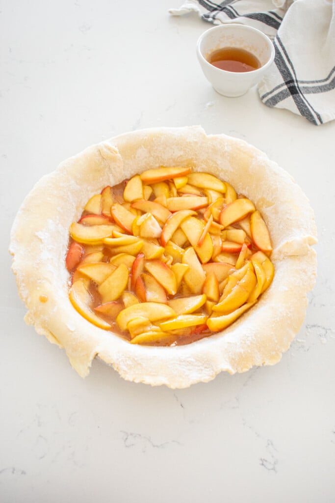honey lemon apple pie filling in a raw pie crust in a pie pan on a marble counter.