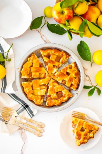 honey lemon apple pie with a lattice top cut into slices on a white marble counter with fresh lemons and apples.