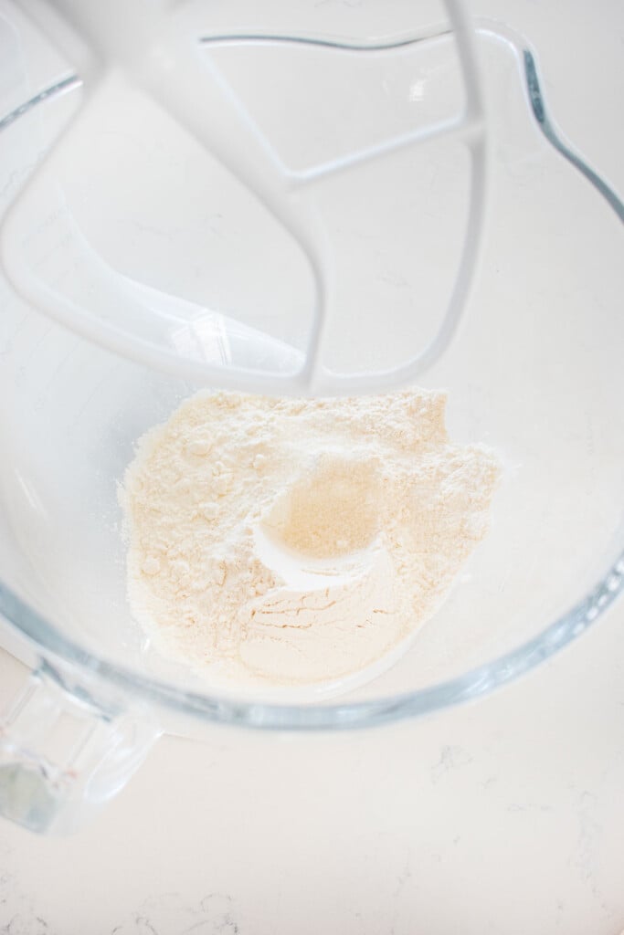 glass mixing bowl with all purpose flour and cane sugar on a marble counter.