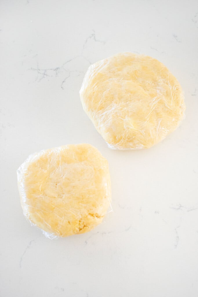top and bottom pie crust wrapped in plastic wrap on a marble counter.