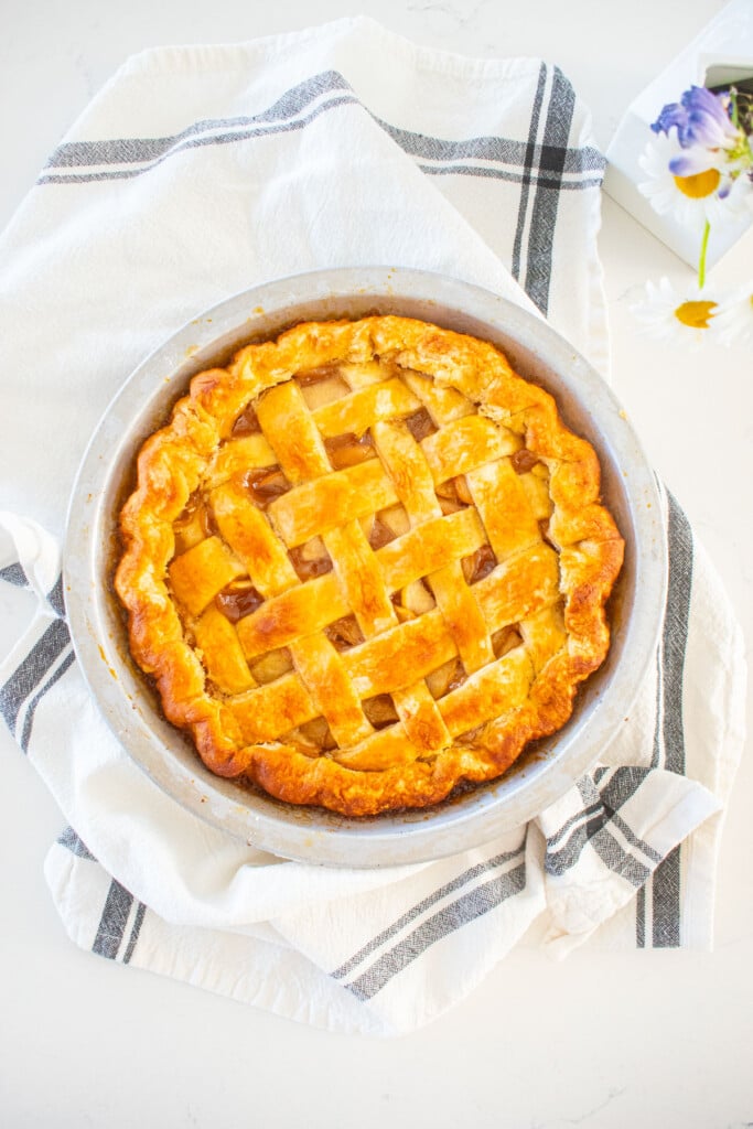 golden brown honey lemon apple pie with a lattice top on a marble counter with fresh flowers.