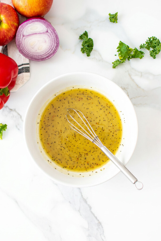 honey mustard salad dressing in a glass mixing bowl on a white marble countertop with a whisk in it.