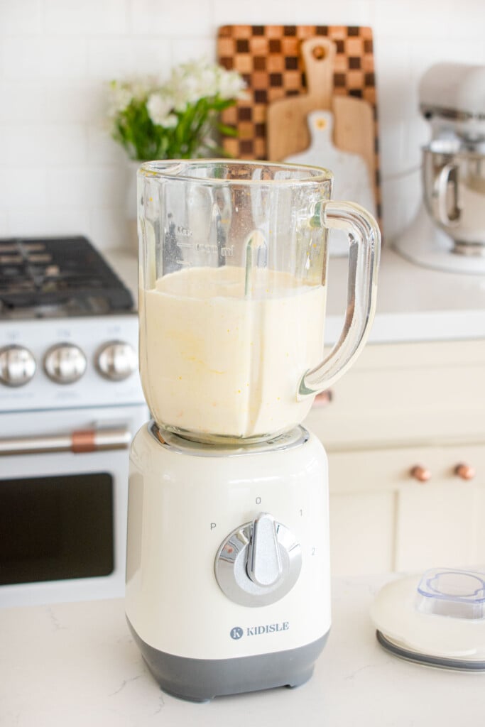 blender with orange creamsicle popsicle mixture in it on a white kitchen counter.