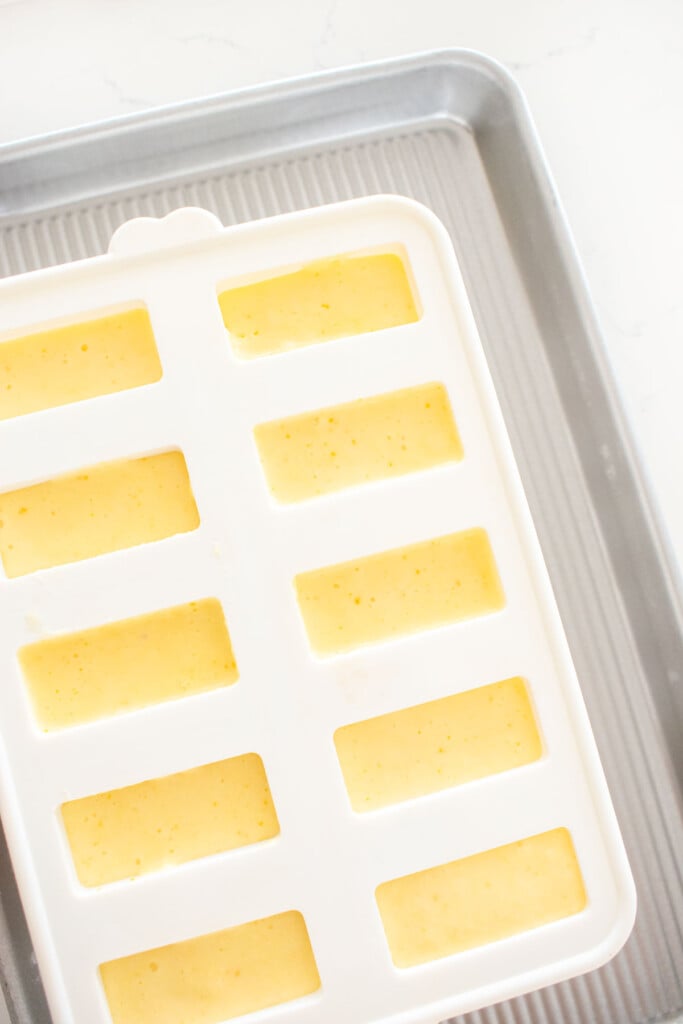 silicone popsicle molds with orange creamsicle popsicle mixture inside.