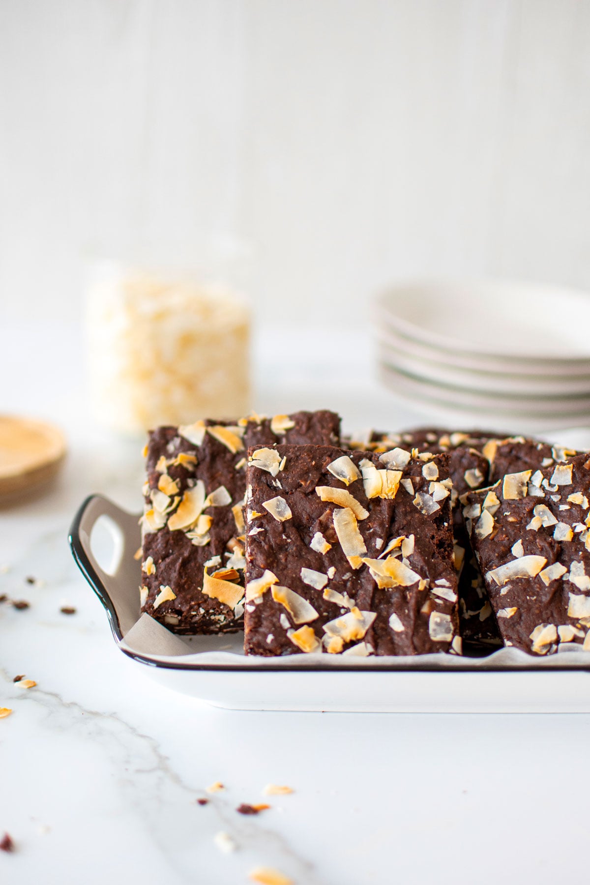 vegan toasted coconut brownies on a white serving platter on a white marble counter.