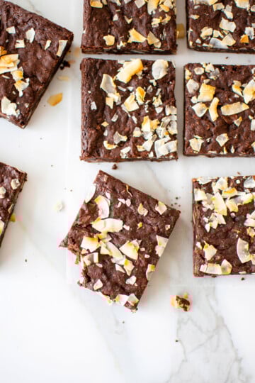vegan toasted coconut brownies on a white marble counter, one brownie with a bite taken out.