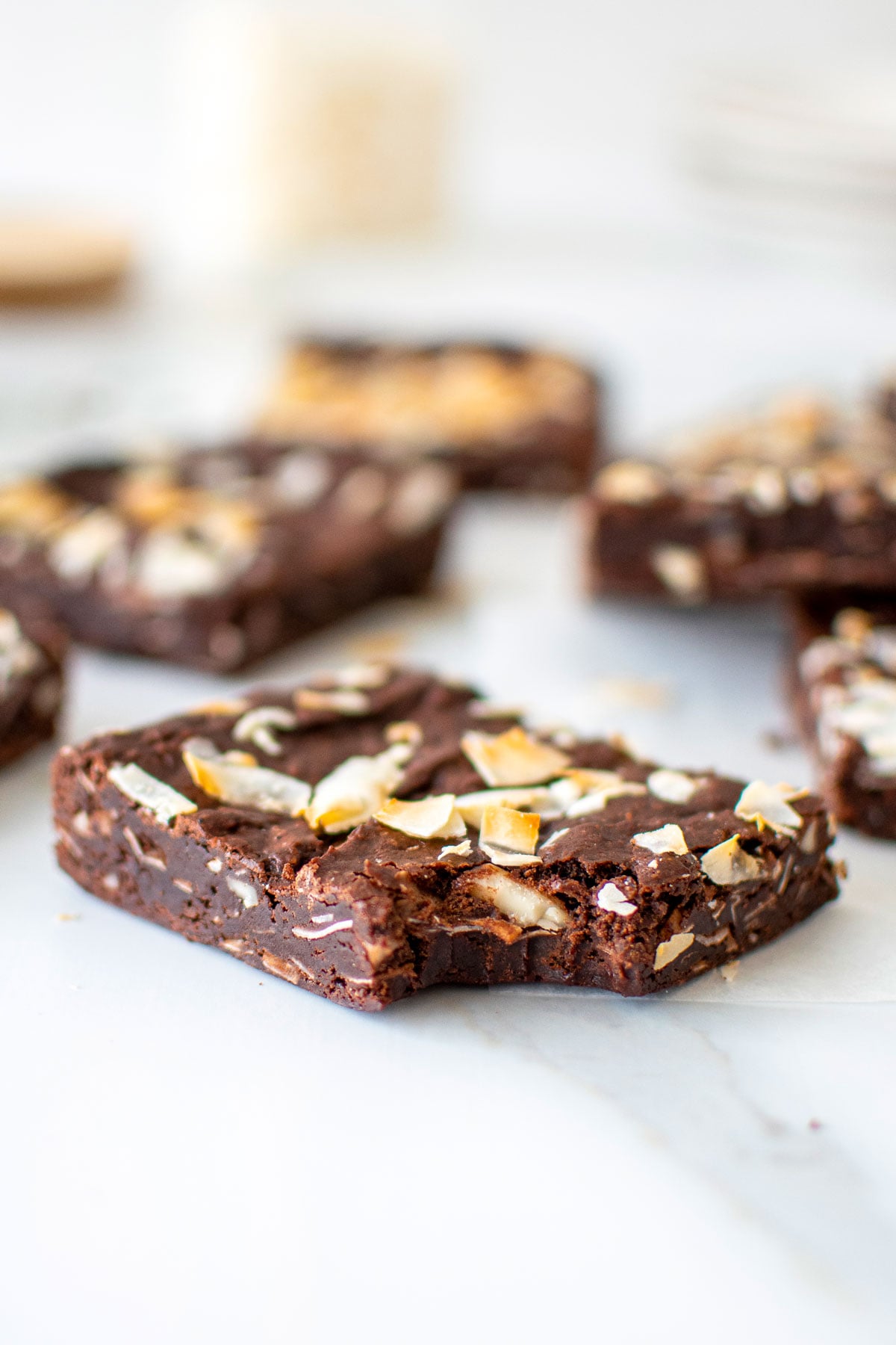 vegan toasted coconut brownie with a bite taken out sitting on a white marble counter.