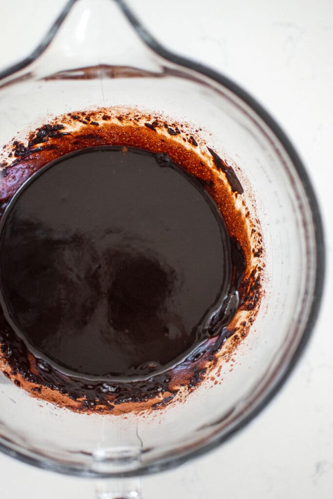 melted chocolate and sugar in a glass mixing bowl on a white marble counter.