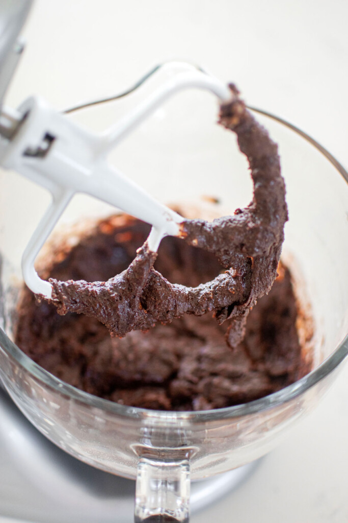 vegan toasted coconut brownie batter in a glass mixing bowl on a white marble counter.