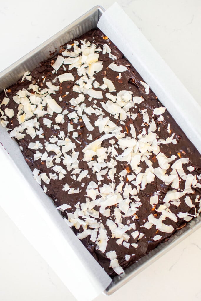 vegan toasted coconut brownie batter spread into a 9x13 inch baking pan on a white marble counter.