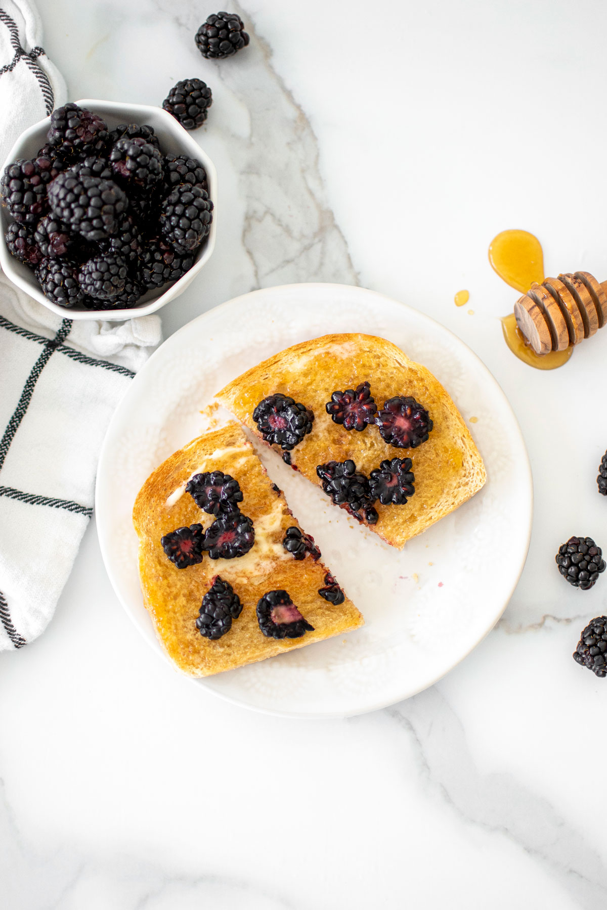 blackberry honey butter toast cut in half on a plate on a marble countertop.