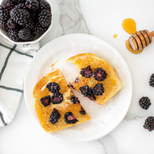 blackberry honey butter toast cut in half on a plate on a marble countertop.