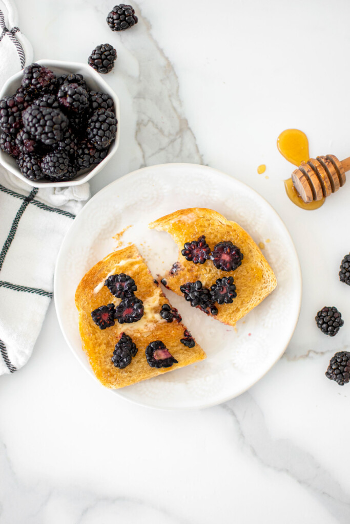 blackberry honey butter toast cut in half on a plate on a marble countertop.