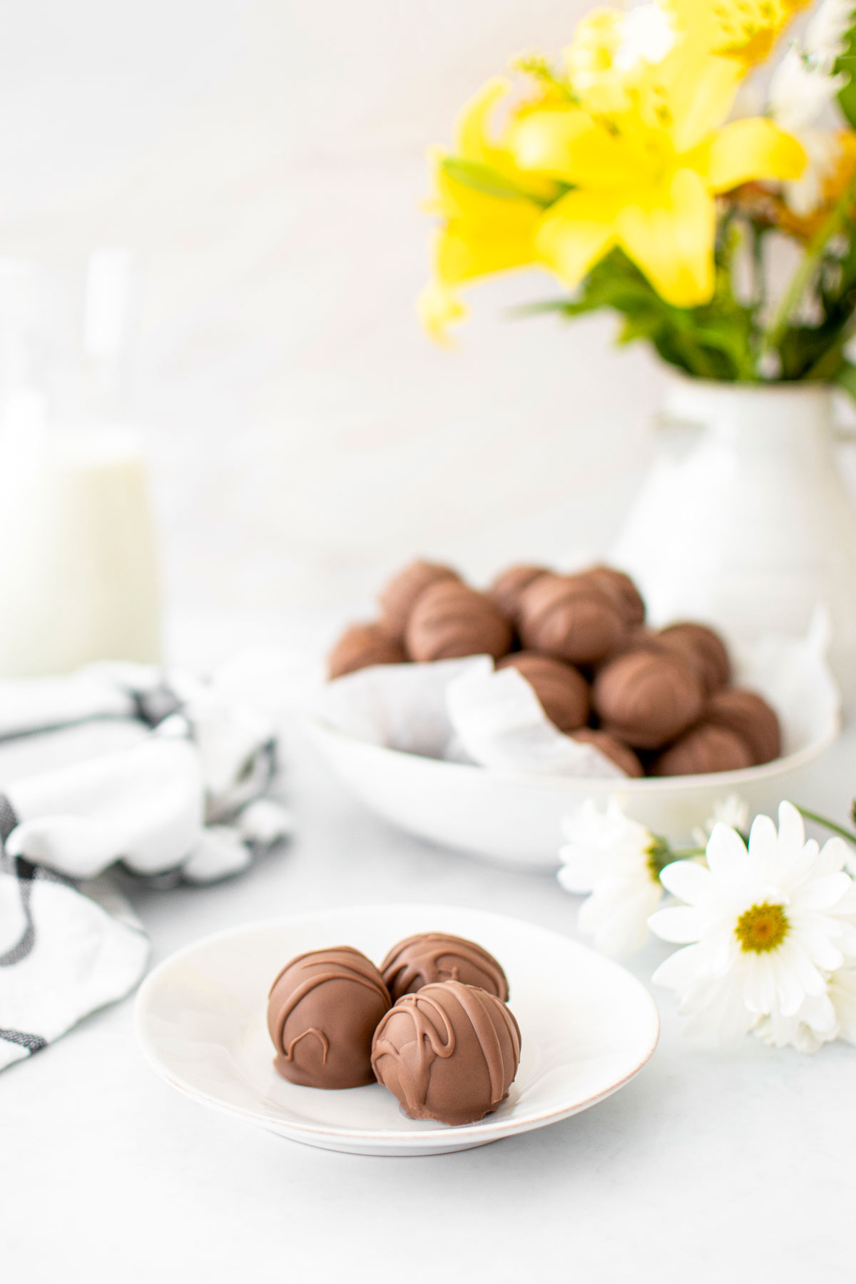 chocolate peanut butter cake balls on a small dessert plate on a white table with a bowl and jug of milk in the background.