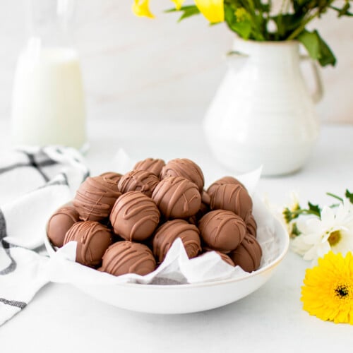 chocolate peanut butter cake balls in a bowl on a white table with fresh flowers.