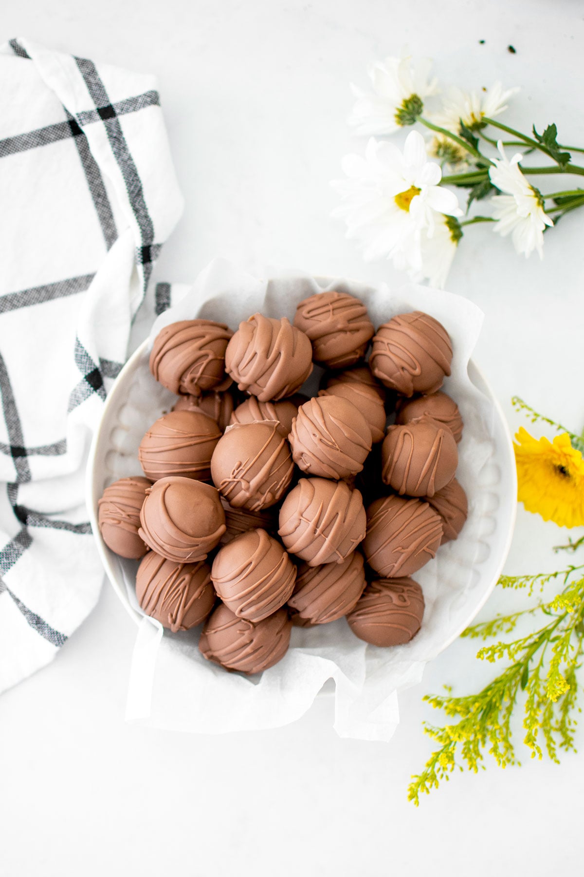 chocolate peanut butter cake balls in a bowl on a white table with fresh flowers.