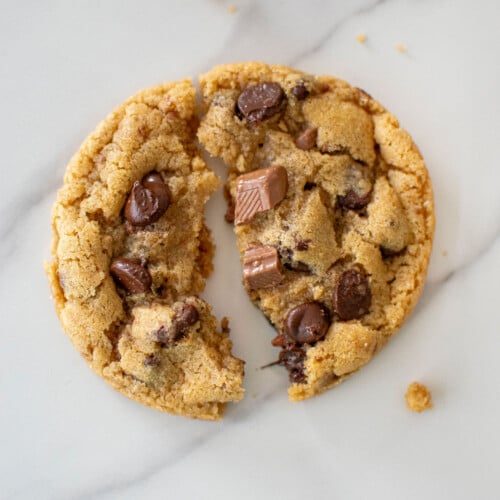 coffee creamer cookie broken in half on a white marble countertop.