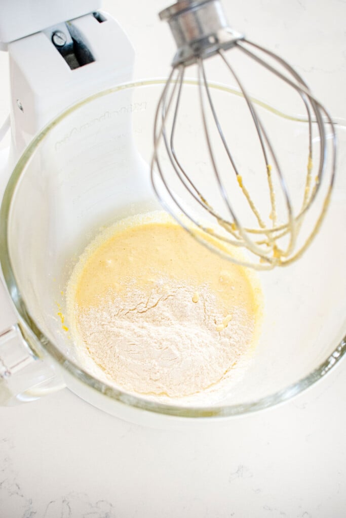 ingredients for homemade custard in a glass mixing bowl on a white marble counter.