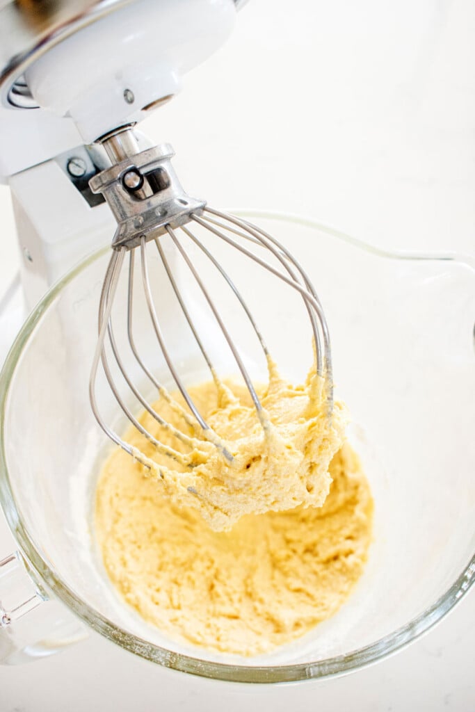 custard being whisked in a glass mixing bowl on a white marble counter.