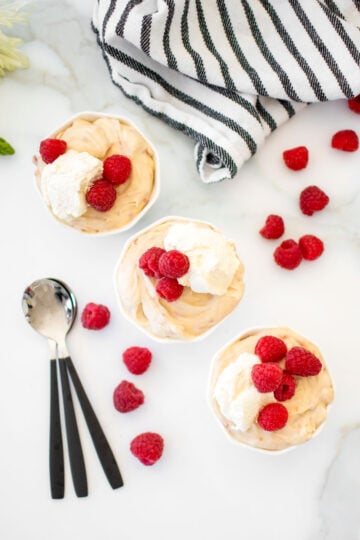 fresh raspberry custard in small white bowls with homemade whipped cream and fresh raspberries on a marble counter.