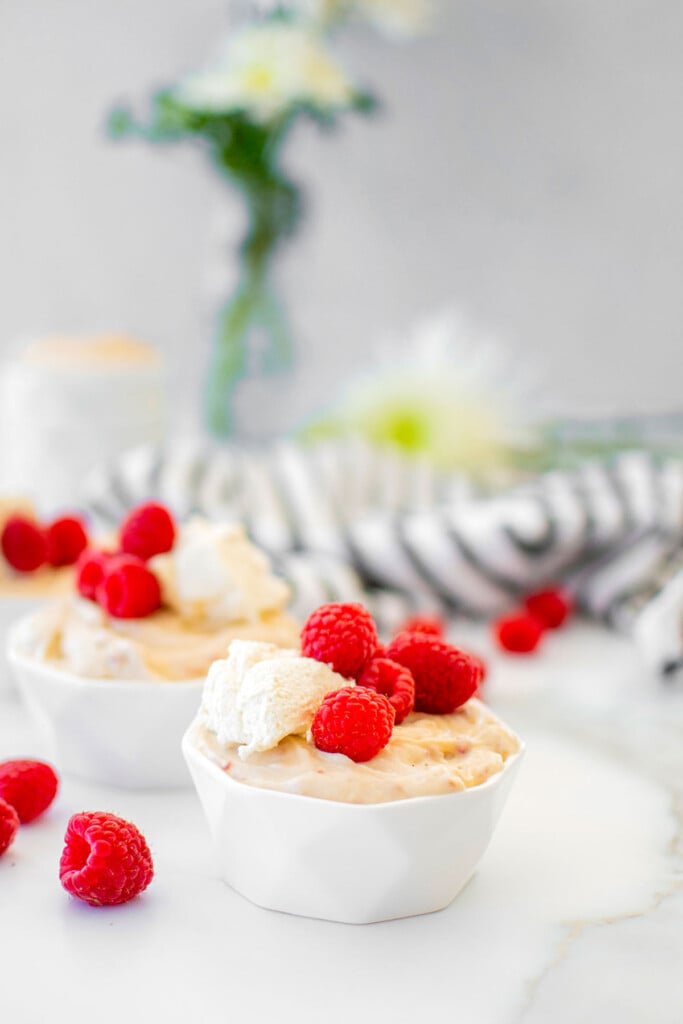 fresh raspberry custard in small white bowls with homemade whipped cream and fresh raspberries on a white marble table.