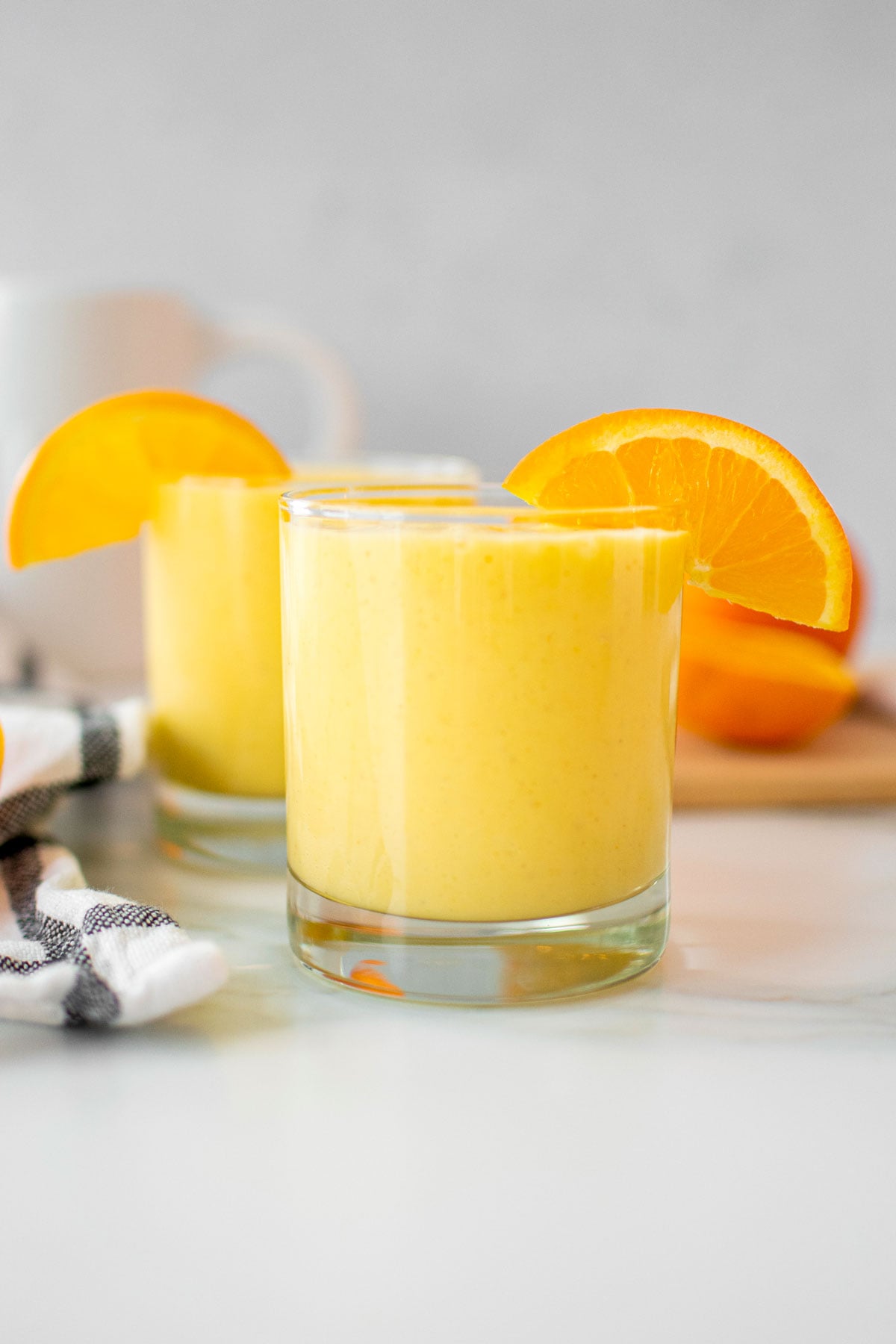 healthy orange julius with protein and an orange slice in a glass on a white marble countertop.