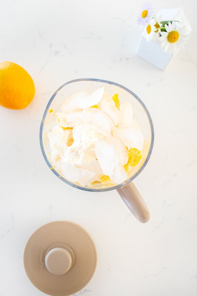 ingredients in blender for orange julius on a marble counter with a fresh orange and flowers.