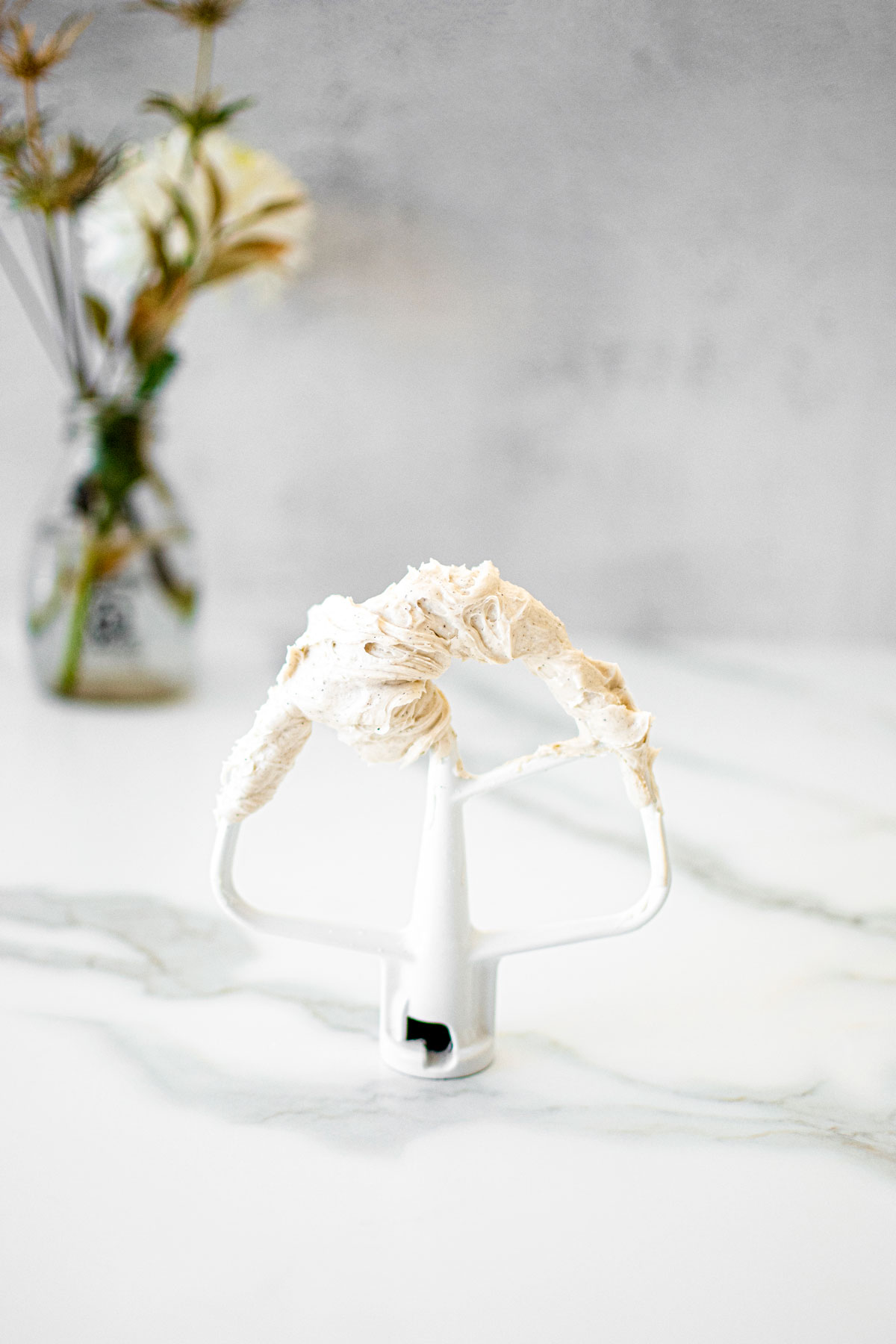 vanilla bean buttercream frosting on a paddle on a white marble counter.