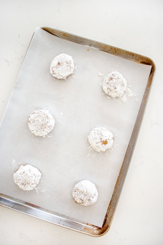 baking sheet with chocolate chip crinkle cookie dough balls rolled in powdered sugar on a baking sheet on a marble counter.