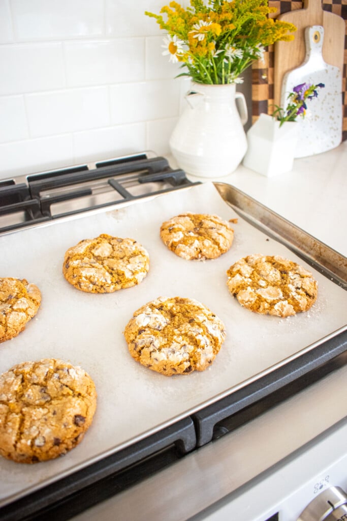 chocolate chip crinkle cookies on a baking sheet cooling on top of an oven.