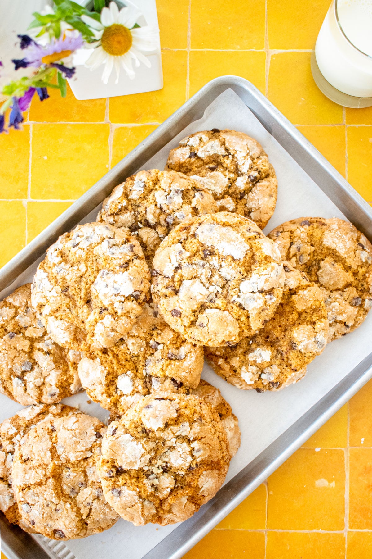baking sheet with chocolate chip crinkle cookies on a yellow tile table with fresh flowers.