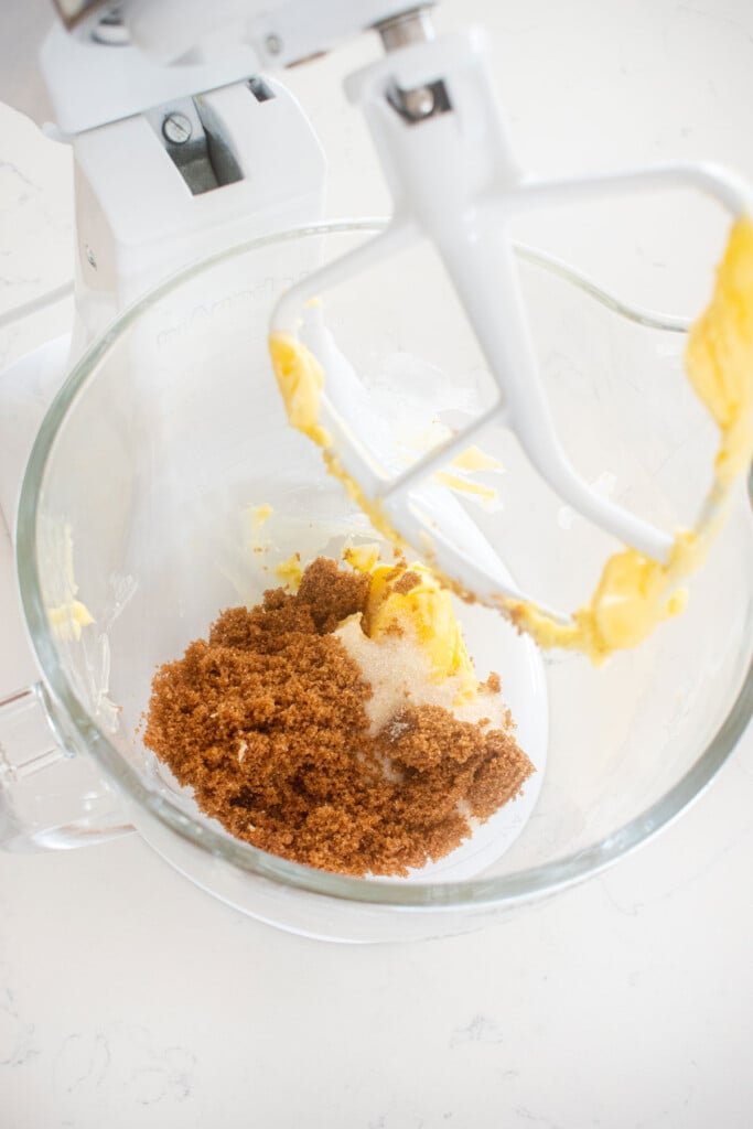 butter and sugars in a glass mixing bowl on a marble counter.