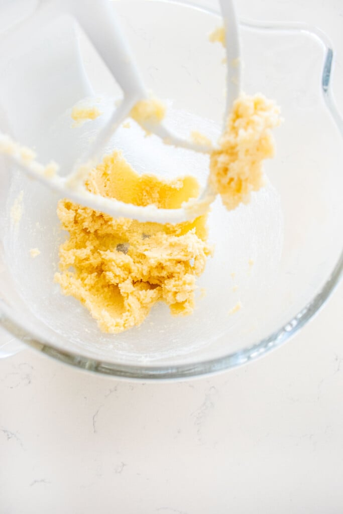 creamed butter and sugar in a glass stand mixing bowl on a white marble counter.