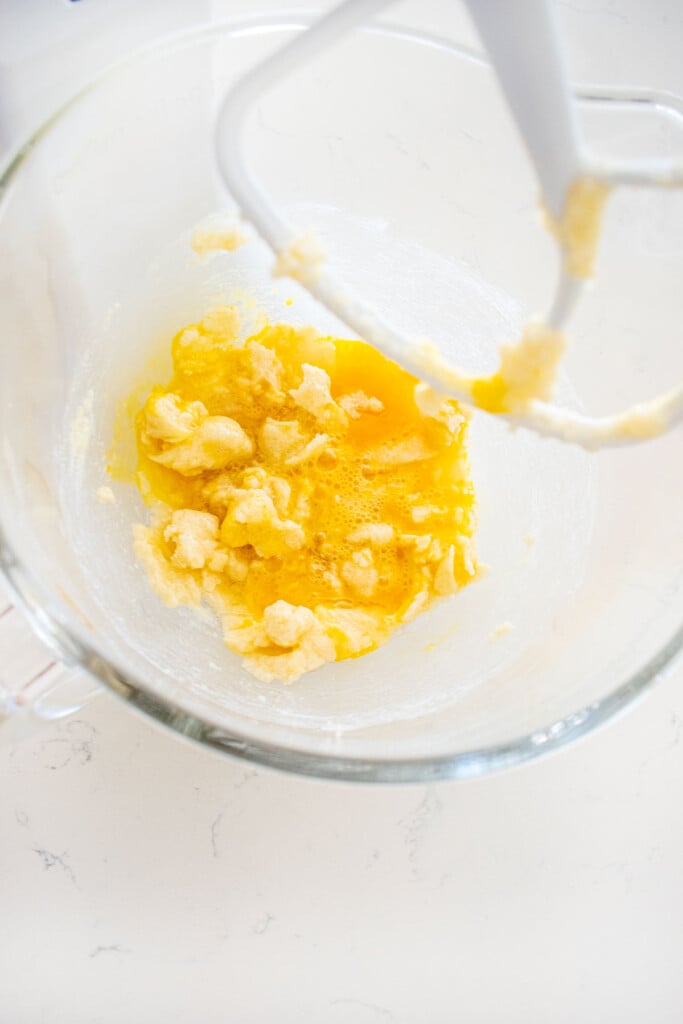 creamed butte and sugar with eggs mixed into it in a glass stand mixing bowl on a white marble counter.