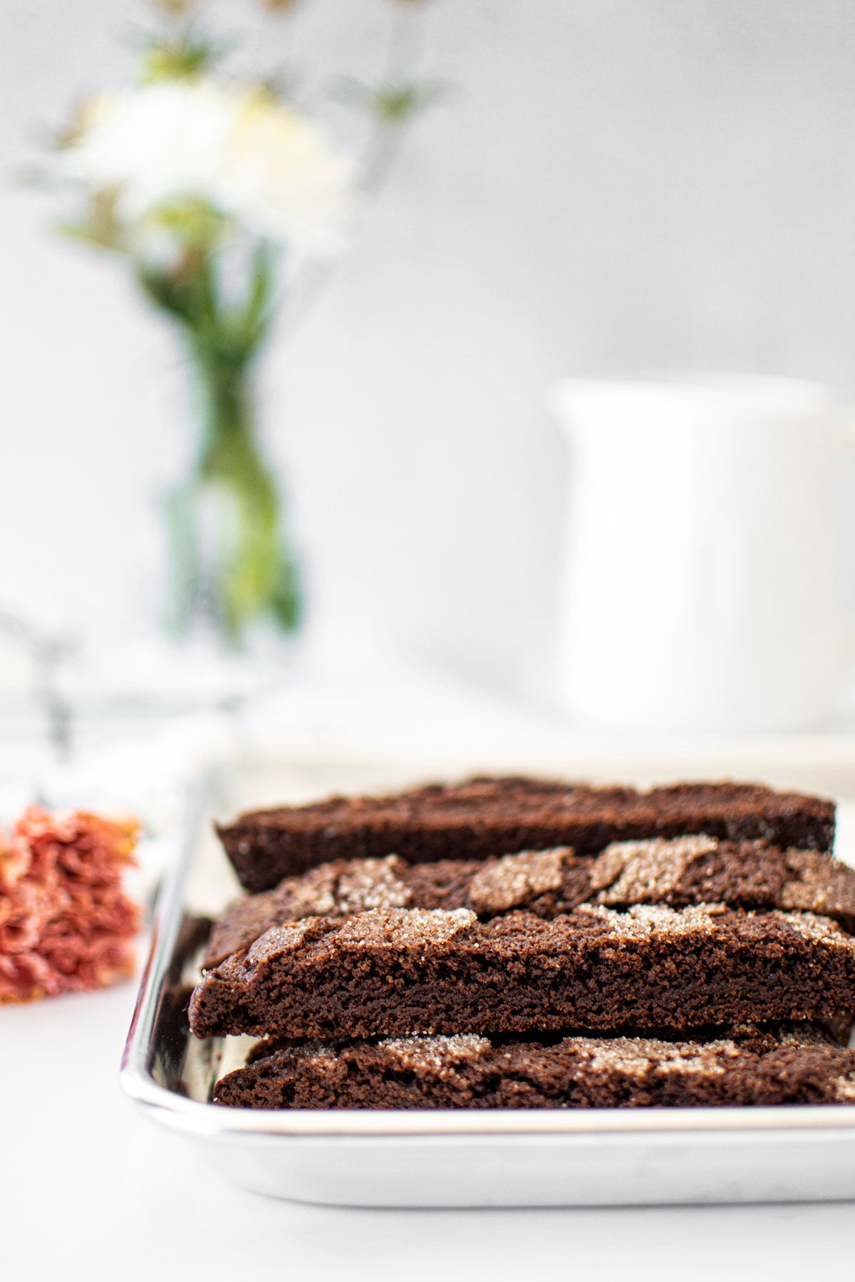 baking sheet of chocolate malt biscotti on a white marble counter with fresh flowers.