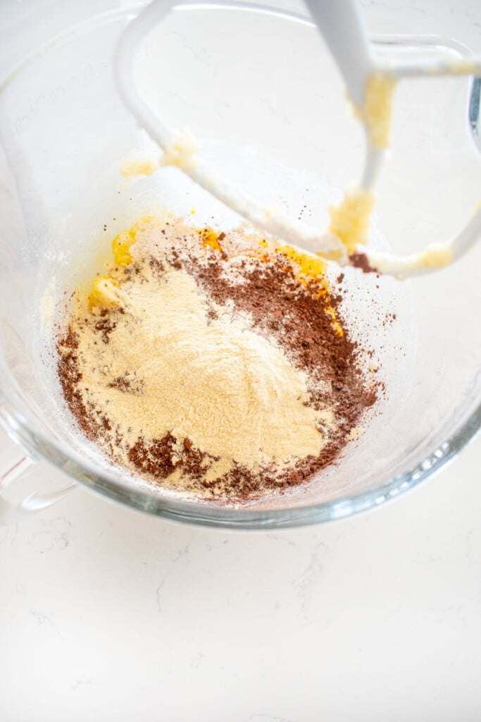 dry ingredients for chocolate malt biscotti added to a glass stand mixing bowl on a white marble counter.