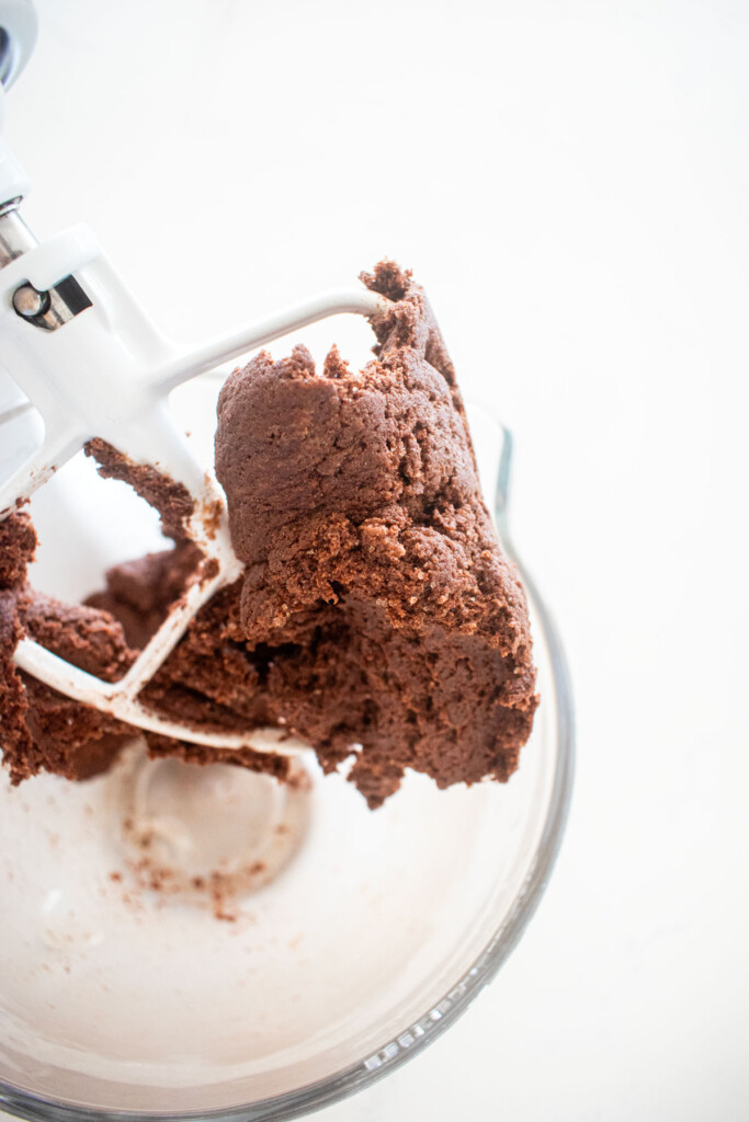 chocolate malt biscotti cookie dough in a glass stand mixing bowl on a white marble counter.
