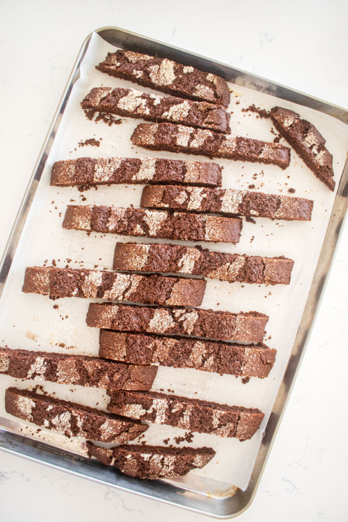 chocolate malt biscotti sliced into pieces on a baking sheet on a marble counter.