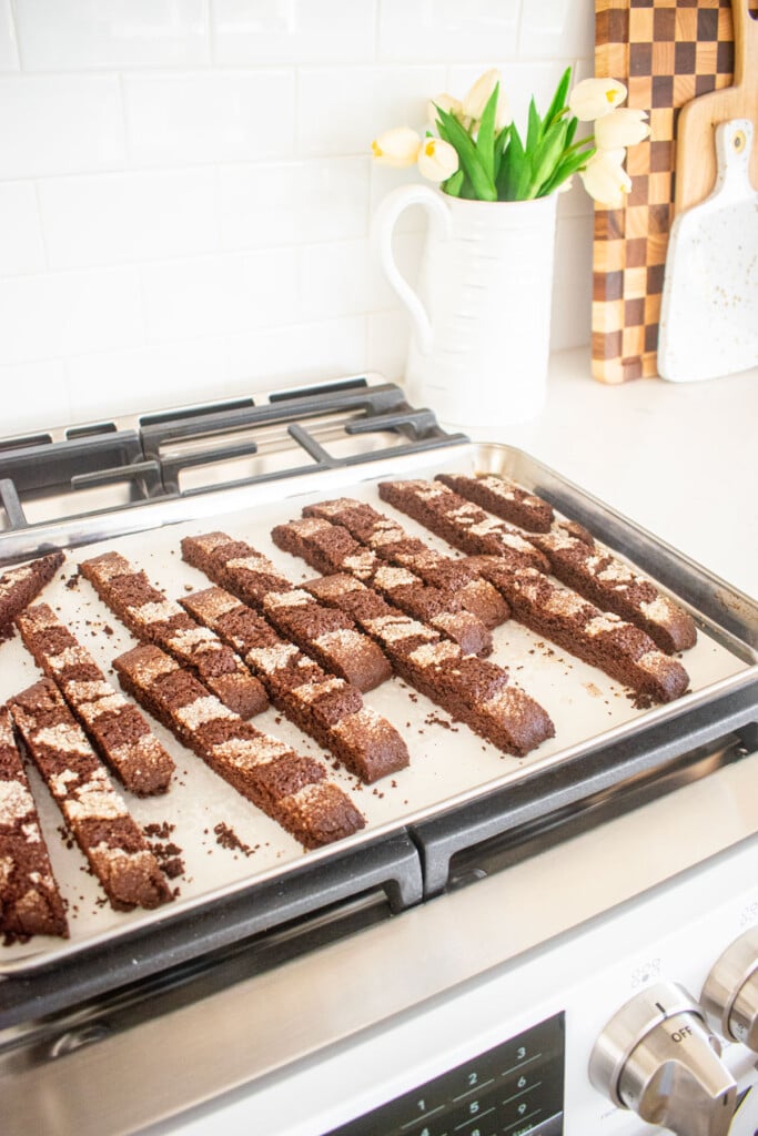chocolate malt biscotti cooling on a baking sheet on top of an oven.