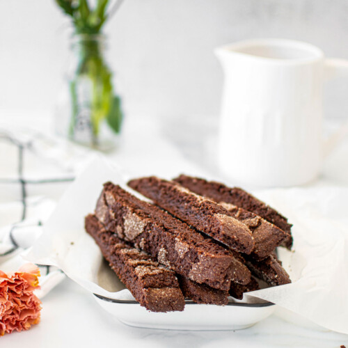 chocolate malt biscotti in a white serving platter on a white marble counter.