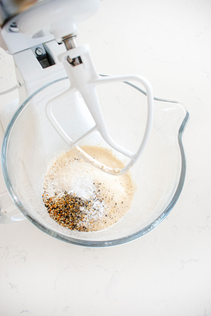 flour, sugar, and everything bagel seasoning in a glass mixing bowl on a white countertop.
