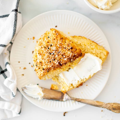 everything bagel scone cut in half with cream cheese on a white plate on marble countertop.